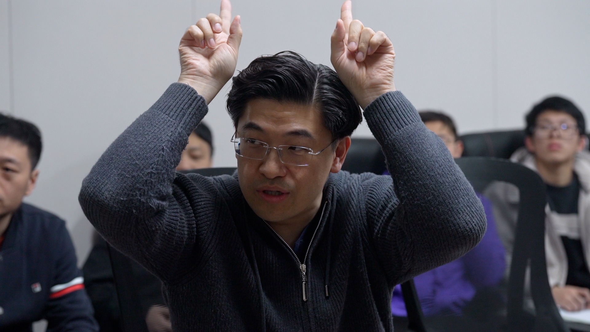 Zhang Shaofu demonstrates a character's posture during a company meeting. /CGTN