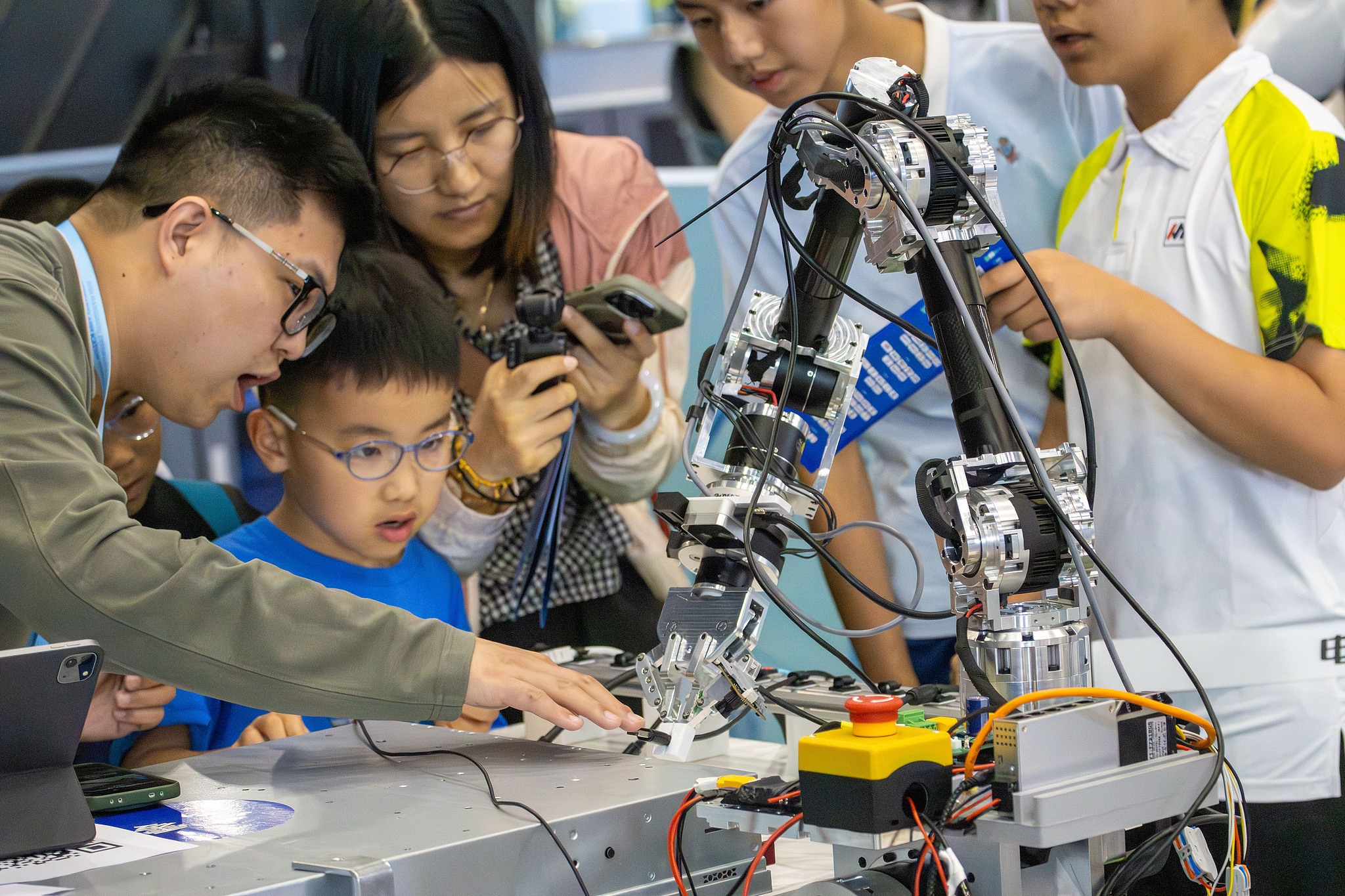An engineer guides children in operating robotic arms at the 2026 Hangzhou International Embodied Robot Scenario Application Competition in Hangzhou, east China's Zhejiang Province, May 16, 2026. /VCG
