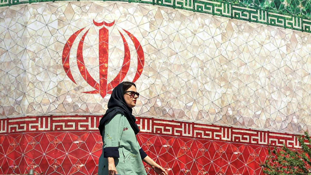 A woman walks past a billboard displaying Iran's national flag in Tehran, Iran, June 14, 2026. /VCG