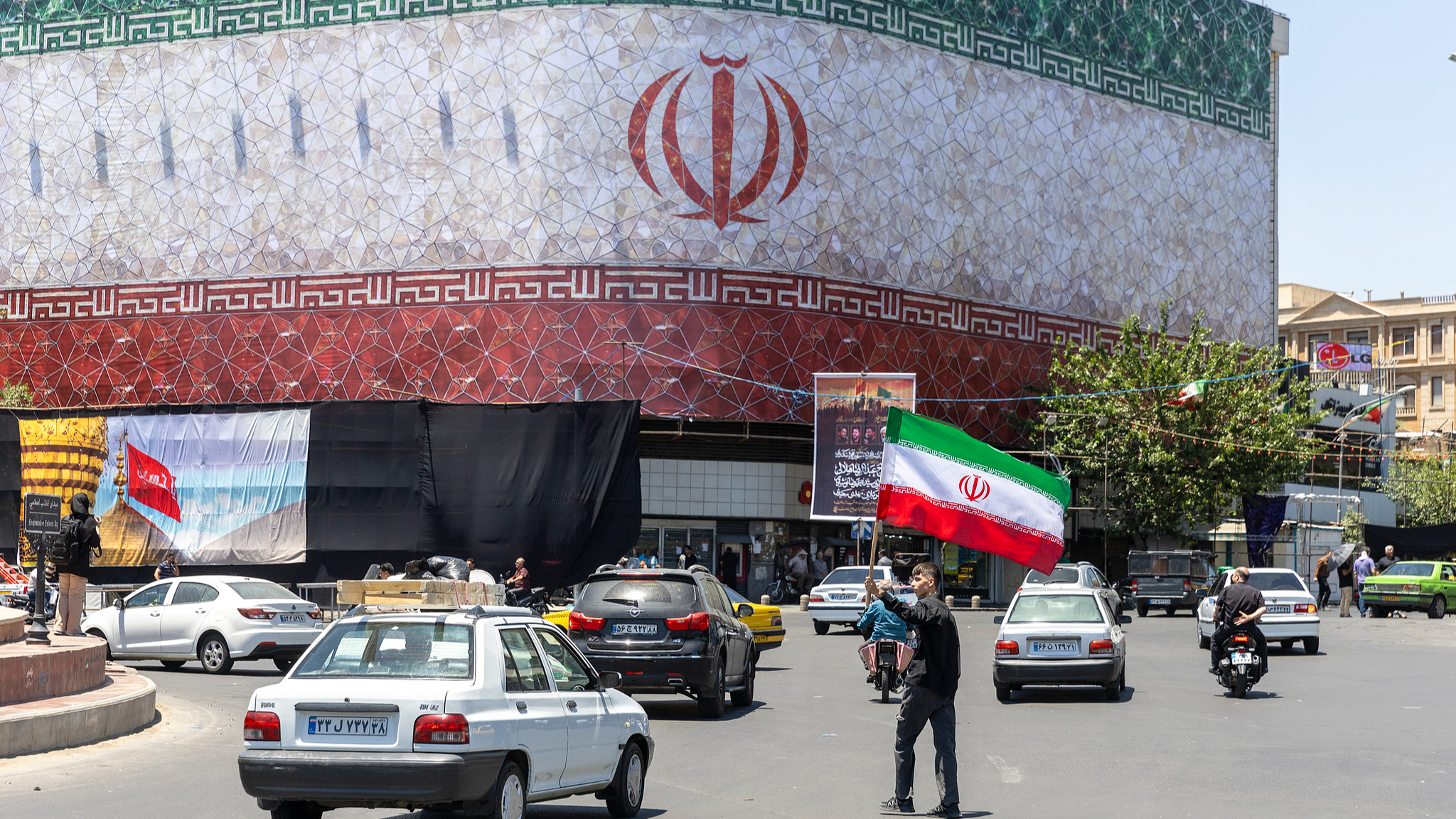 A man waves an Iranian flag in front of a billboard displaying the Iranian flag after the US and Iran signed a preliminary agreement to end the war, Tehran, Iran, June 15, 2026. /VCG