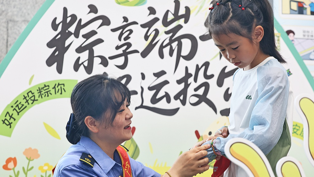 A staff worker at a railway station wears a five-colored string bracelet, which is believed to protect people from evil spirits and bring good luck, to a girl in Jiaxing City, east China's Zhejiang Province, June 18, 2026. /VCG