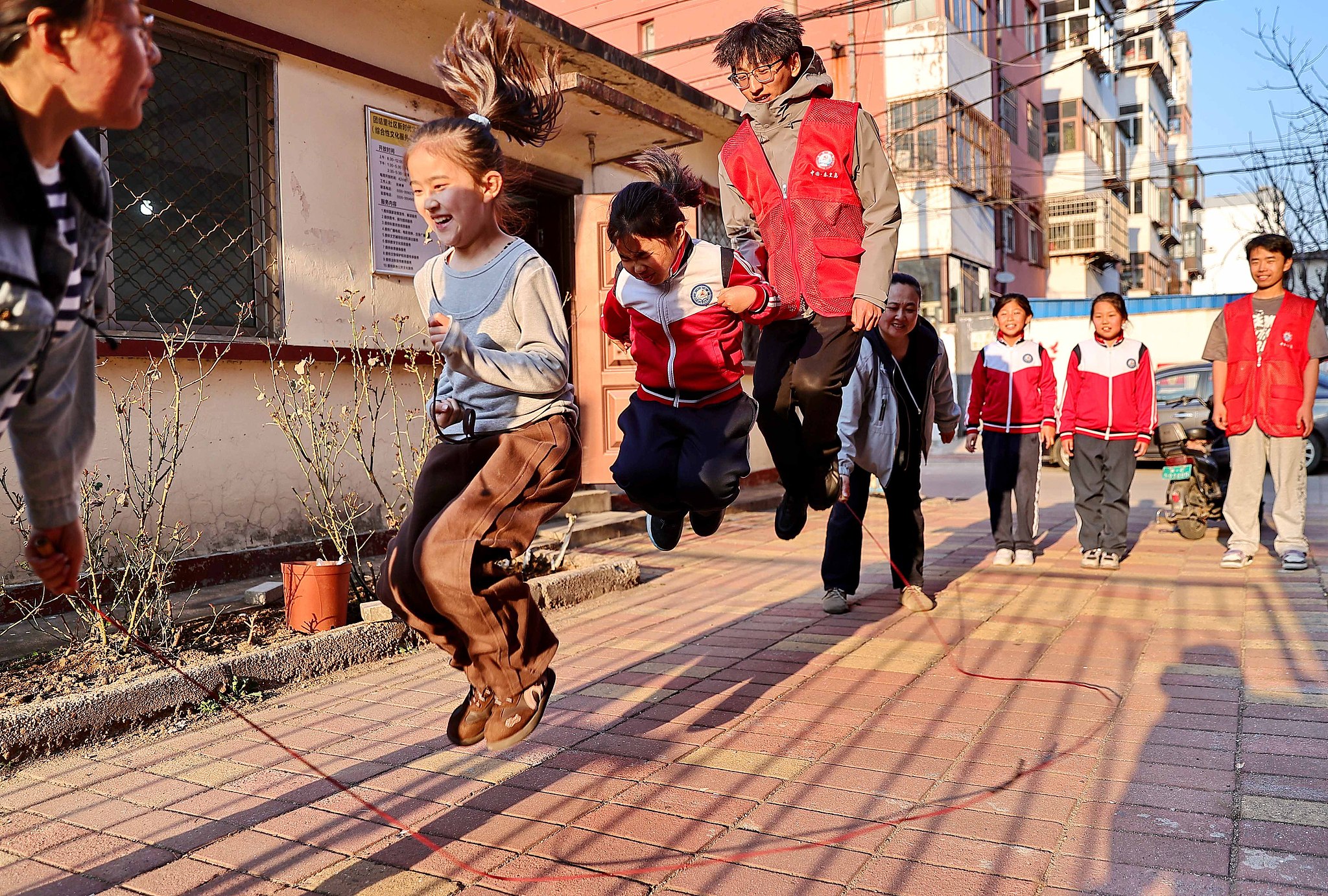 At a community after-school activity center in Qinhuangdao, Hebei Province, college student volunteers and children jump rope together. /VCG 