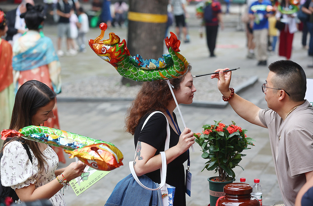A staff at the Beijing Folk Custom Museum is seen drawing the characters on an international visitor's forehead, a custom symbolizing best wishes for safety, well-being and success, Beijing, China, June 19, 2026. /VCG
