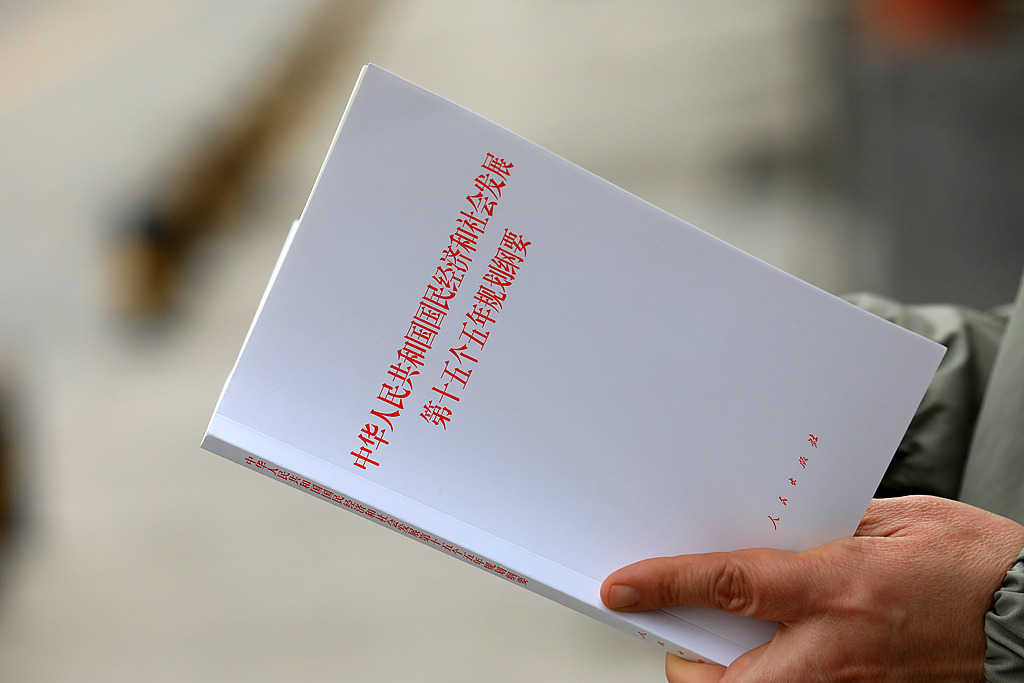 A resident stands reading a single-volume copy of the Outline of the 15th Five-Year Plan for National Economic and Social Development of the People's Republic of China, in Anyang City, Henan Province, March 23, 2026. /VCG