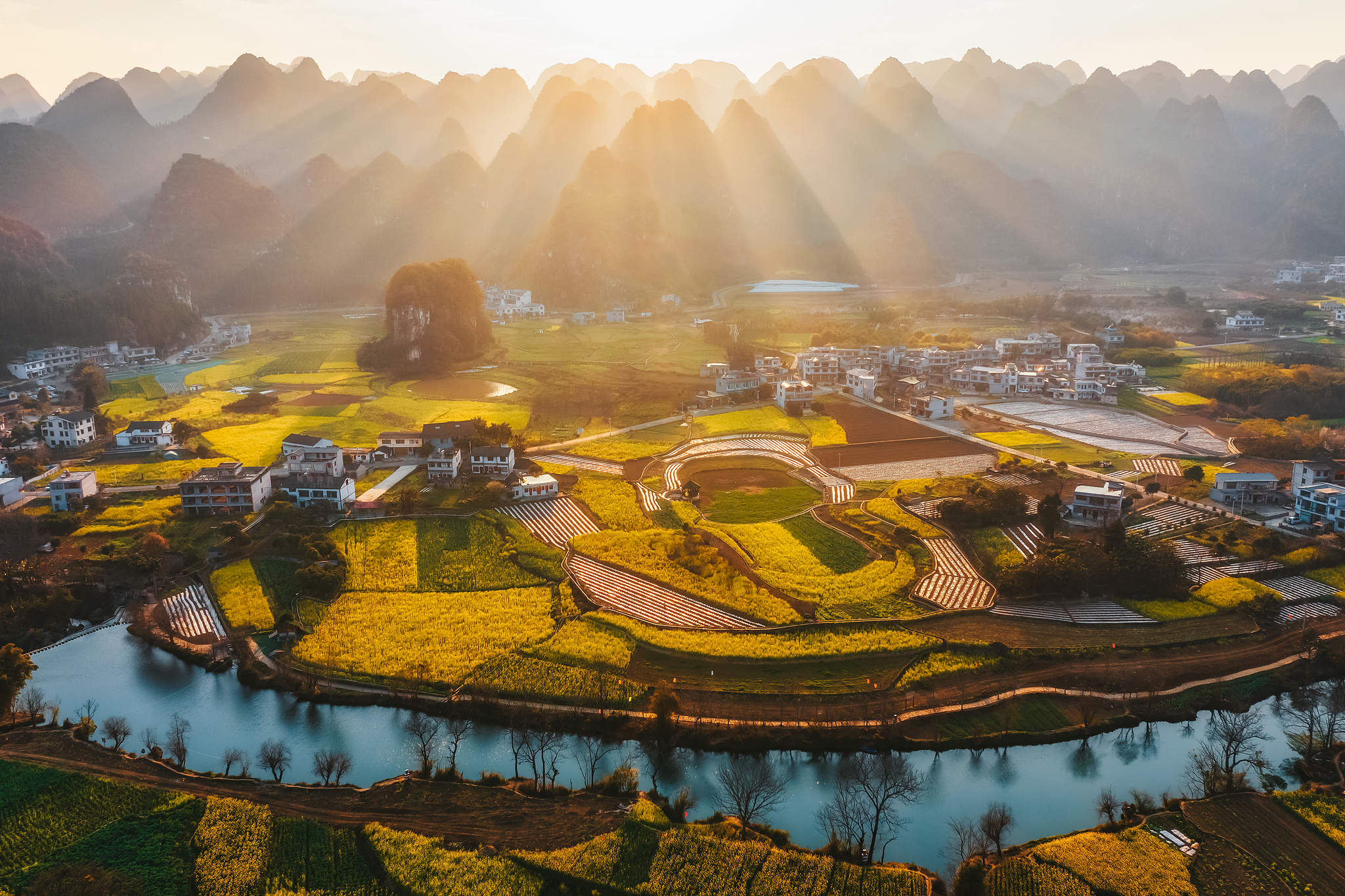 Sun rays shine over rapeseed fields and karst hills in the Qianxinan Bouyei and Miao Autonomous Prefecture, Guizhou Province, southwest China. /VCG