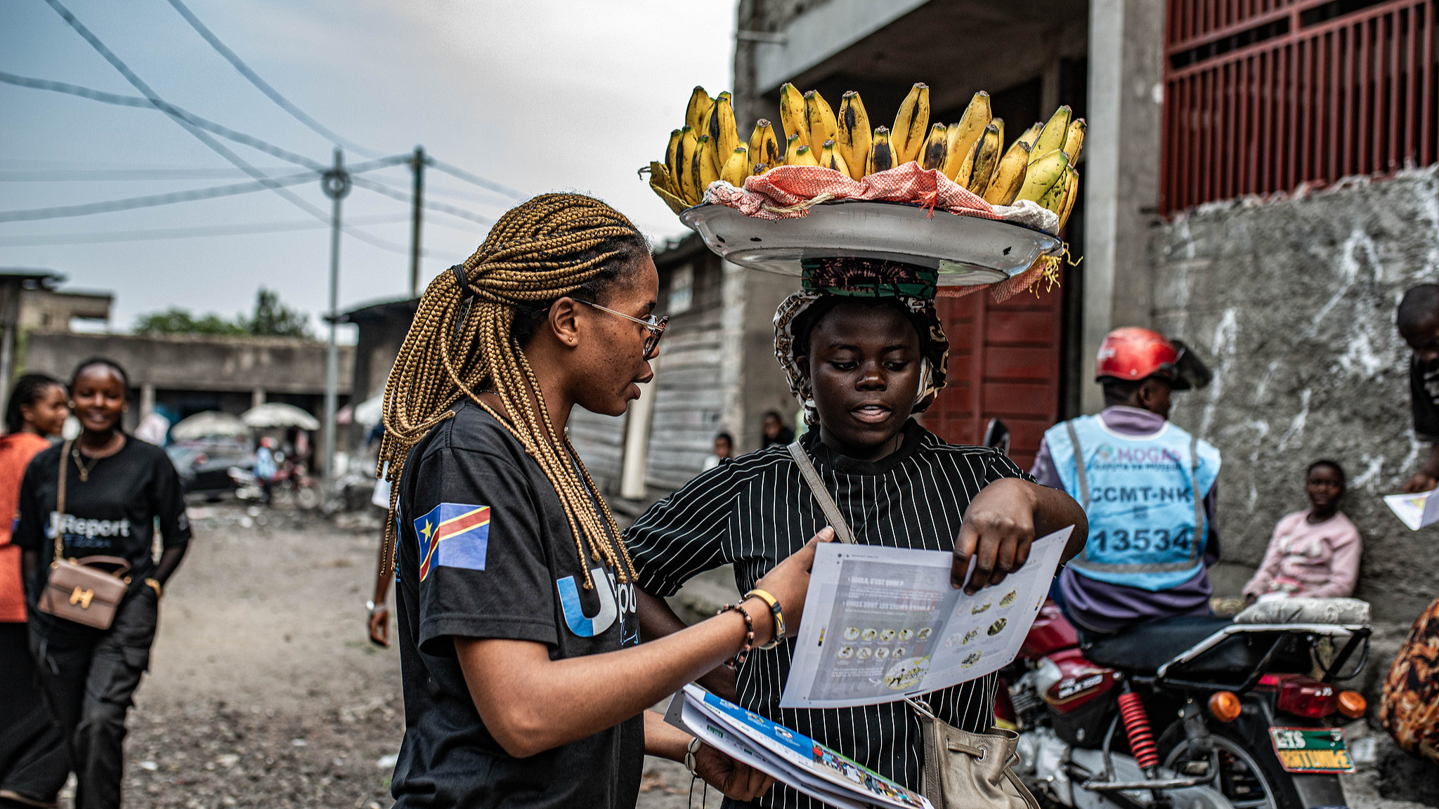 A woman carrying plantains reads a pamphlet as staff with UNICEF's 