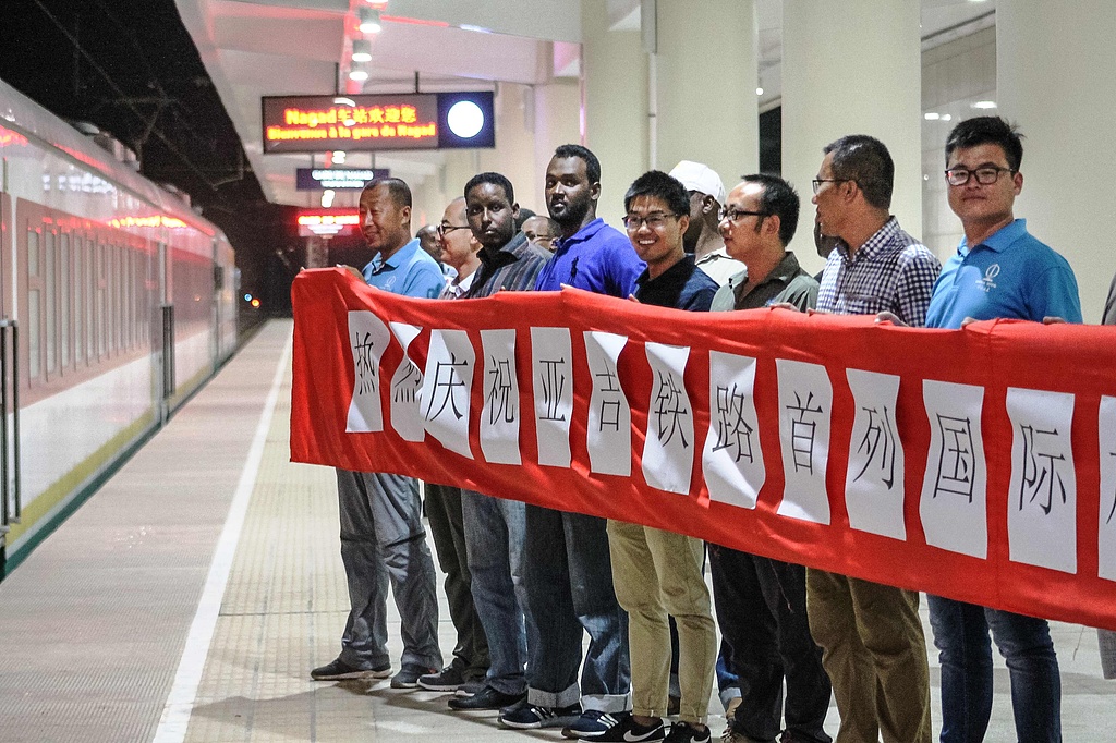 Workers of a Chinese construction company hold a banner to welcome the first commercial train as it arrives at a platform at Nagad railway station in Djibouti on January 3, 2018. /VCG