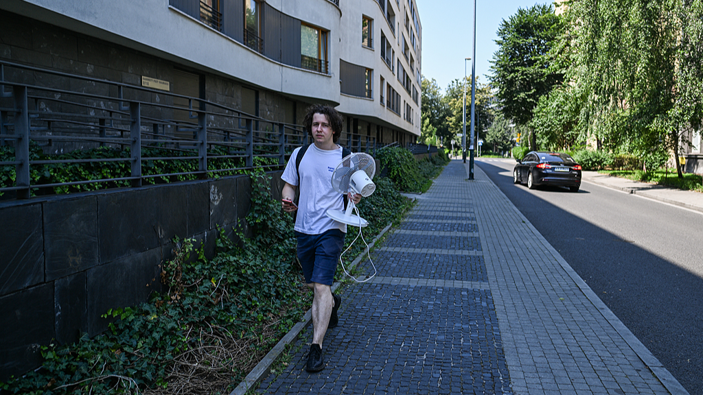 A man carries a electric fan while he walks home as high temperatures continue in Krakow, Poland, June 28, 2026. /VCG