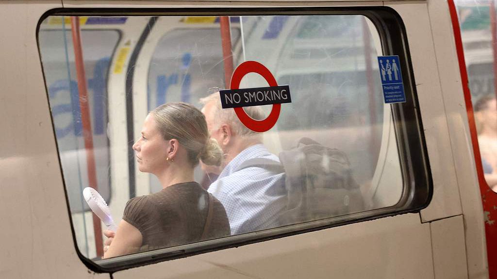 A commuter uses a fan in an attempt to cool down on a London Underground tube carriage, UK, June 23, 2026. /VCG