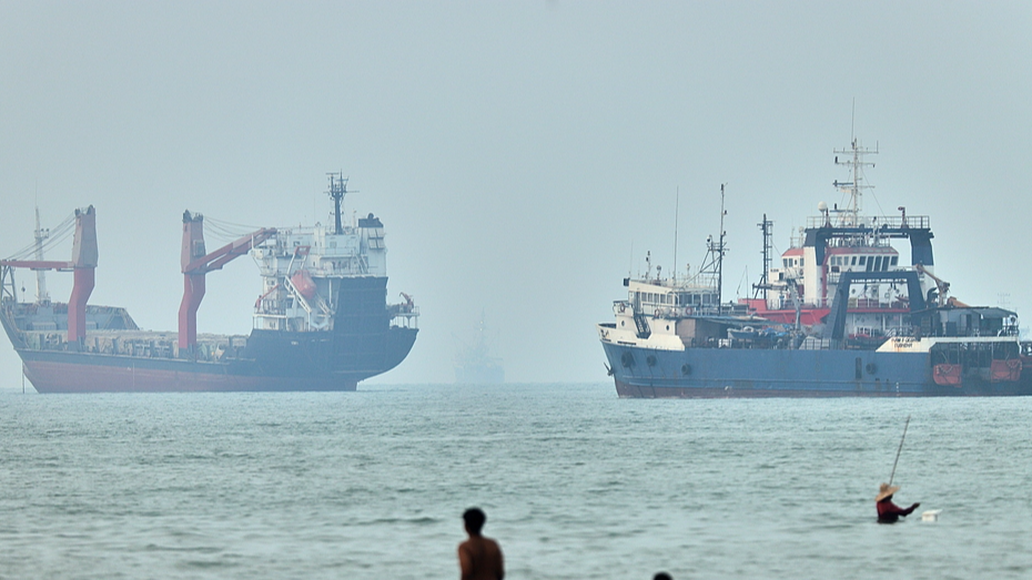 Locals wade through the water as cargo ships sit at anchor in the Strait of Hormuz near Bandar Abbas, Iran, June 30, 2026. /VCG