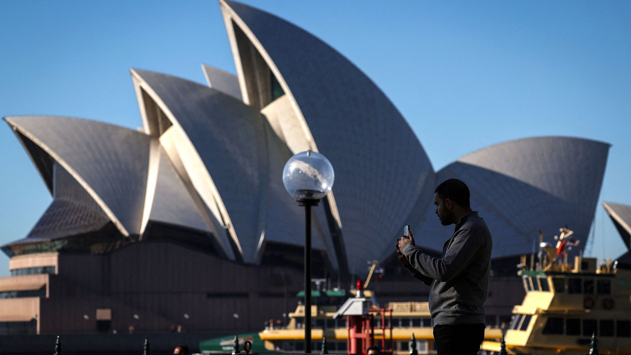 A tourist takes pictures in front of the Sydney Opera House in Sydney, Australia, June 23, 2025. /CFP