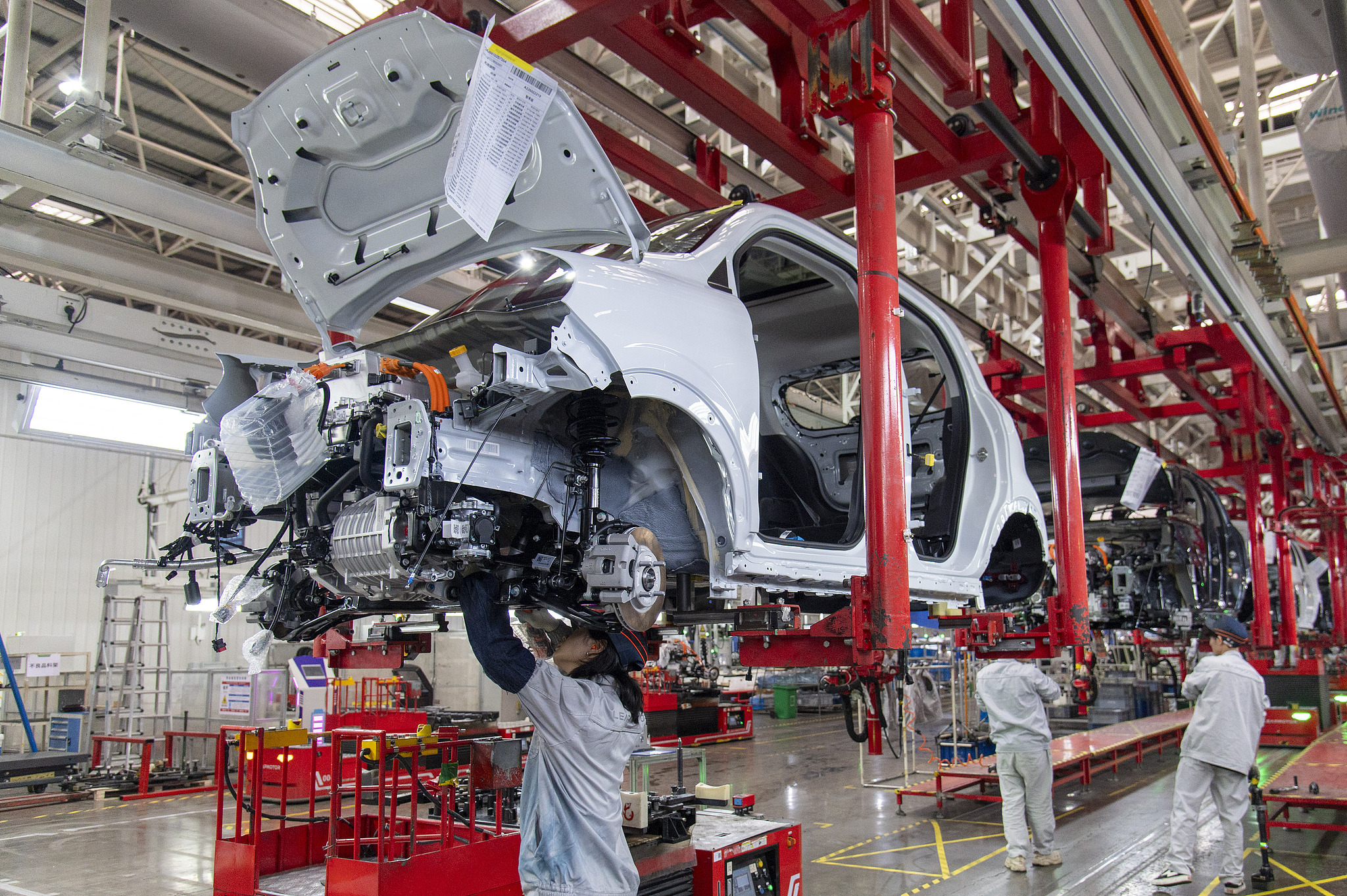 Workers fit components into an electric vehicle at a manufacturing plant. /VCG