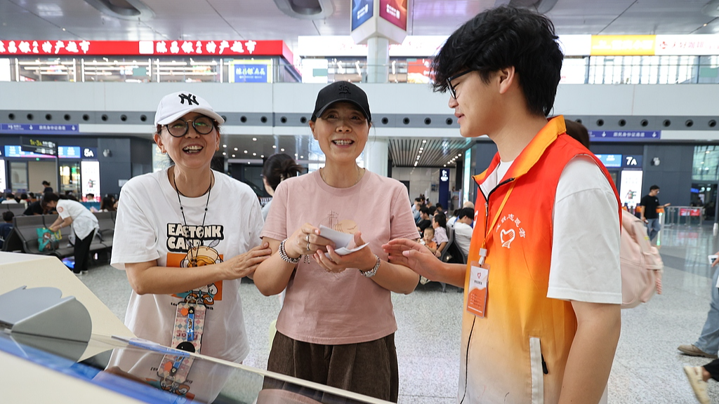 A young volunteer helps older women with ticket purchases at a train station, southwest China's Chongqing Municipality, July 23, 2026. /VCG