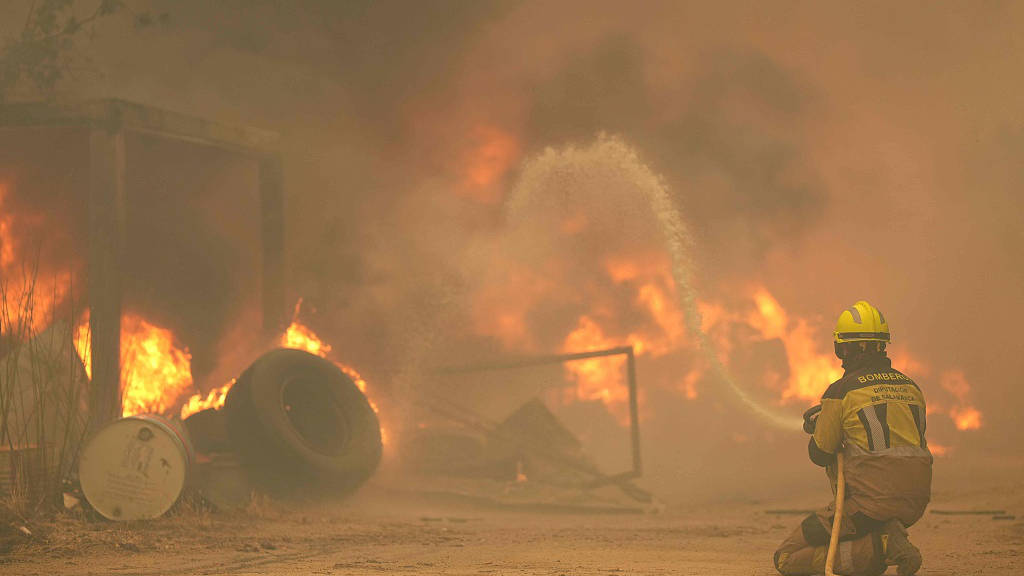 A firefighter sprays water on burning tires and barrels while battling a wildfire in the Cebreros area, near Avila, 80 kilometers west of Madrid, July 24, 2026. /VCG