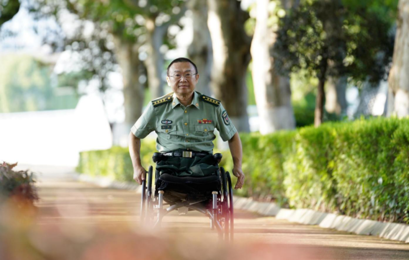 Wang Ji pushes a wheelchair along a tree-lined path on the NUDT campus. (Photo: Xinhua)