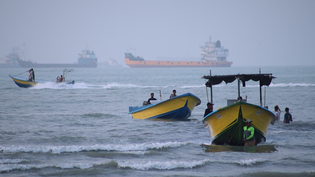 Small boats line the shore as cargo ships and other commercial vessels are anchored in the Strait of Hormuz off Bandar Abbas, Iran, July 27, 2026. /VCG