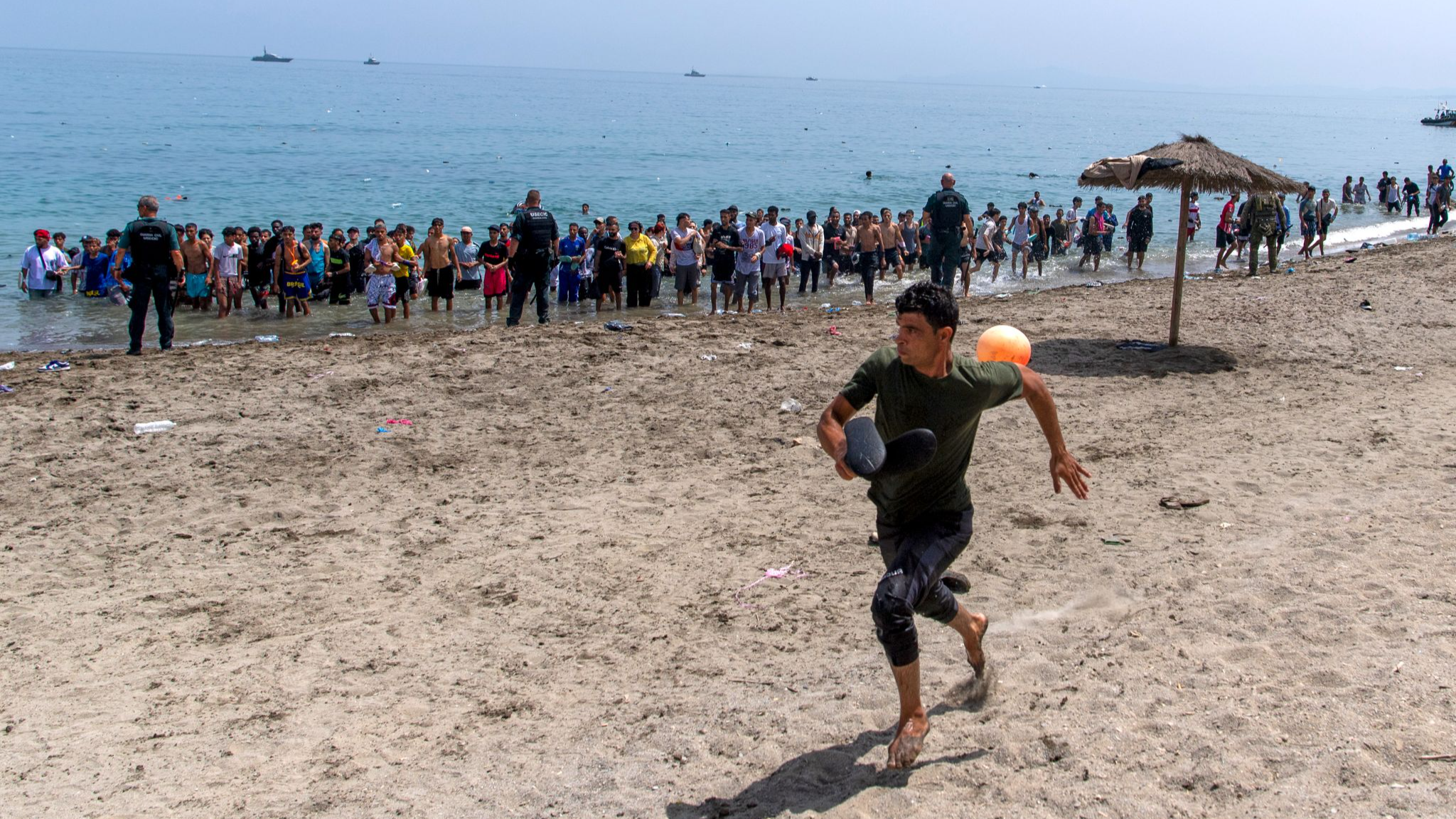A migrant runs from Spanish police officers as they cordon off access to the beach for people crossing from Morocco into the Spanish enclave of Ceuta, July 31, 2026. /AP