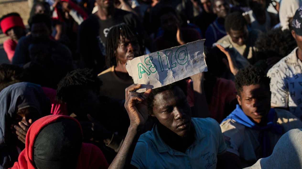 An immigrant who crossed from Morocco into the Spanish enclave of Ceuta holds a sign reading 