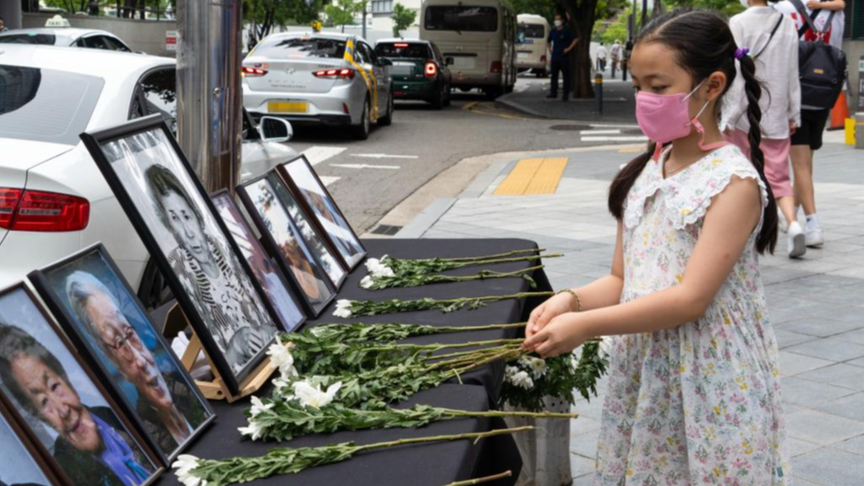A child presents flowers to portraits of 