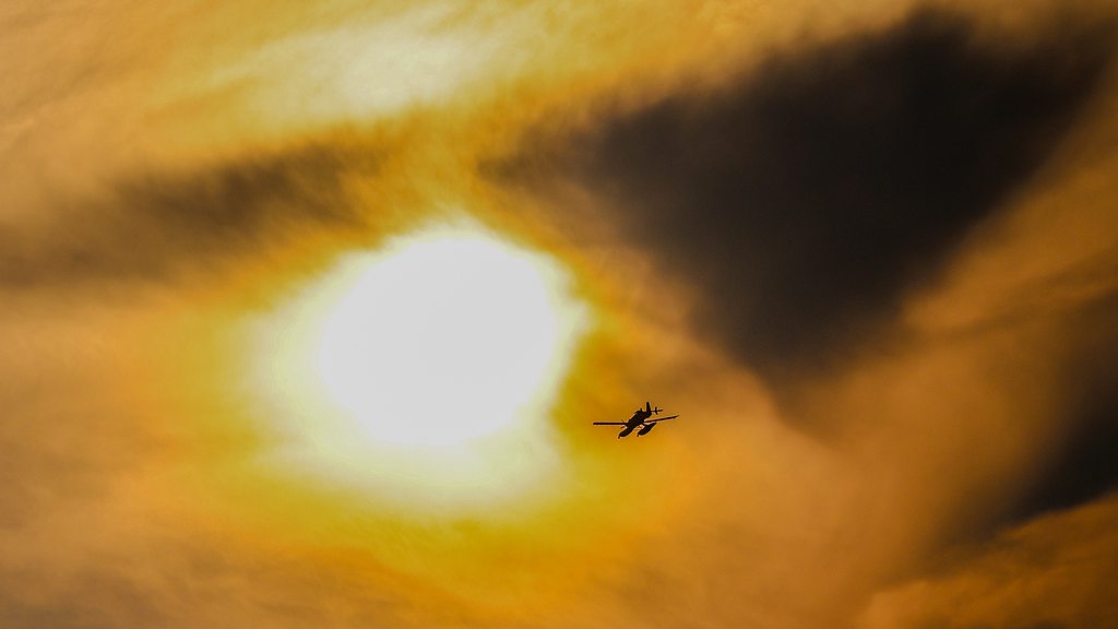 A Swedish firefighting plane flies over the fire zone in the High Fens as dark plumes of smoke block the view of the sun, Sourbrodt, Belgium, August 16, 2026. /VCG