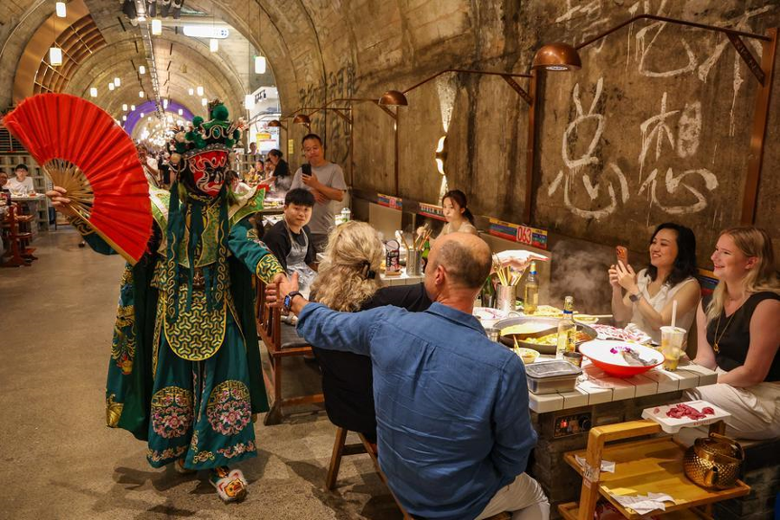 A foreign tourist interacts with a Sichuan Opera performer at a hotpot restaurant housed in a former underground air-raid shelter in Liangjiang New Area of southwest China's Chongqing Municipality, July 10, 2026. /Xinhua