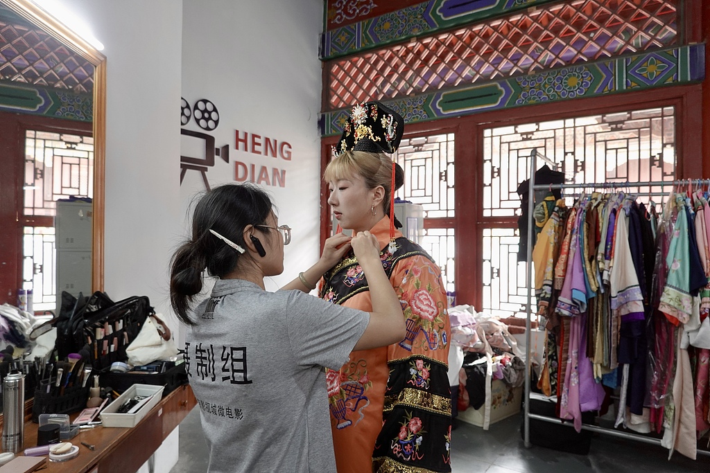 A tourist puts on a costume for a short-drama filming experience at Hengdian World Studios in Zhejiang Province on August 13, 2026. /VCG