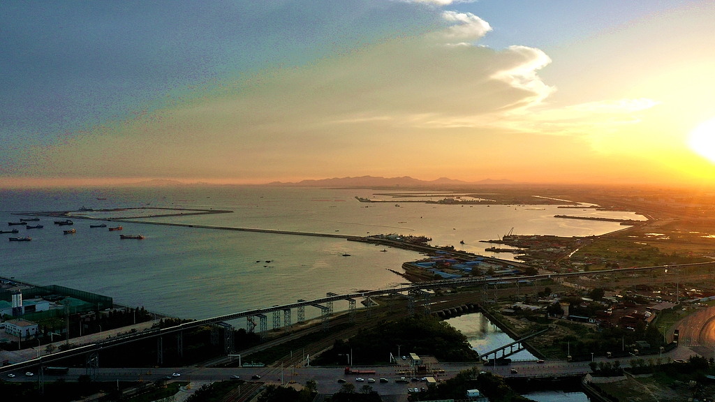 Sunset over the Jinyinshan area in the Port of Rizhao's south operation area, where daily freight trains pass container stacks and cargo-handling equipment, Shandong Province, China, September 25, 2025. /VCG