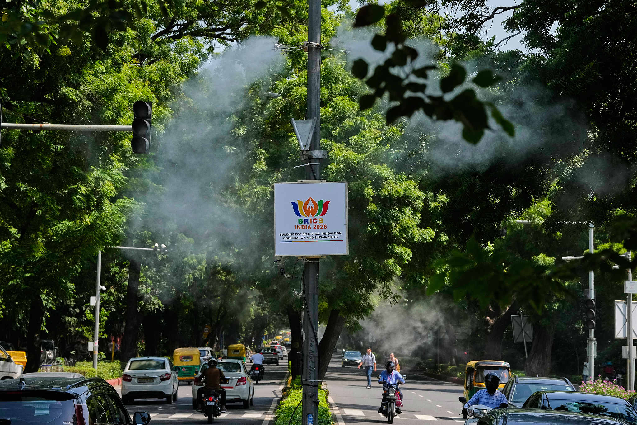 Water-sprinkling jets spray mist to suppress road dust and help curb air pollution as a BRICS summit banner hangs from an electric pole in New Delhi, India, September 10, 2026. /VCG