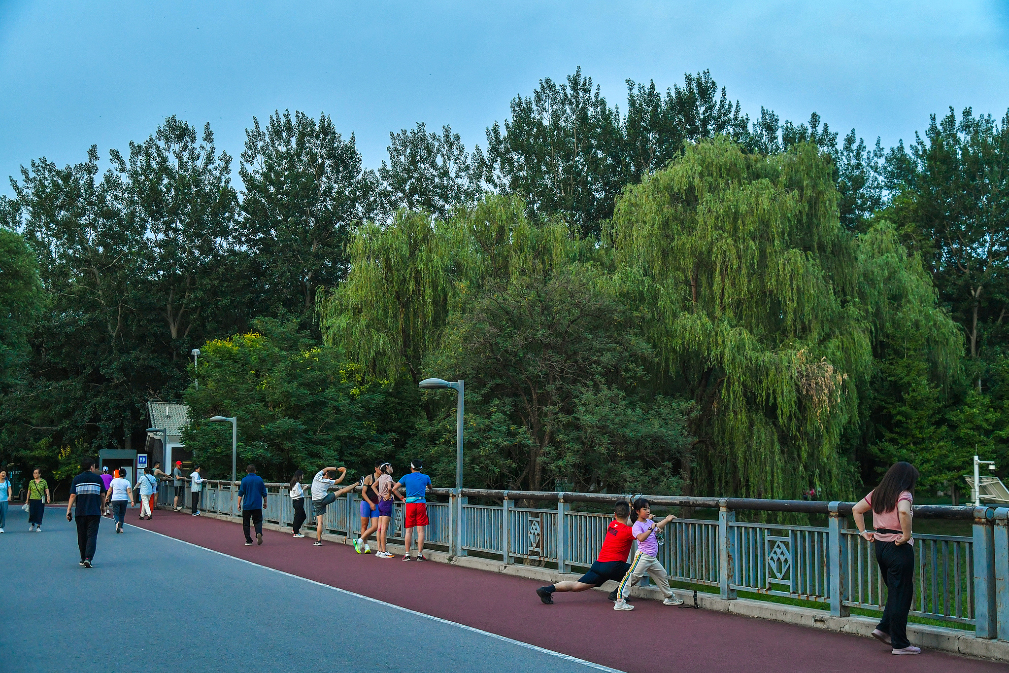 People stroll and stretch along a walkway at Beijing Olympic Forest Park during an evening walk. /VCG