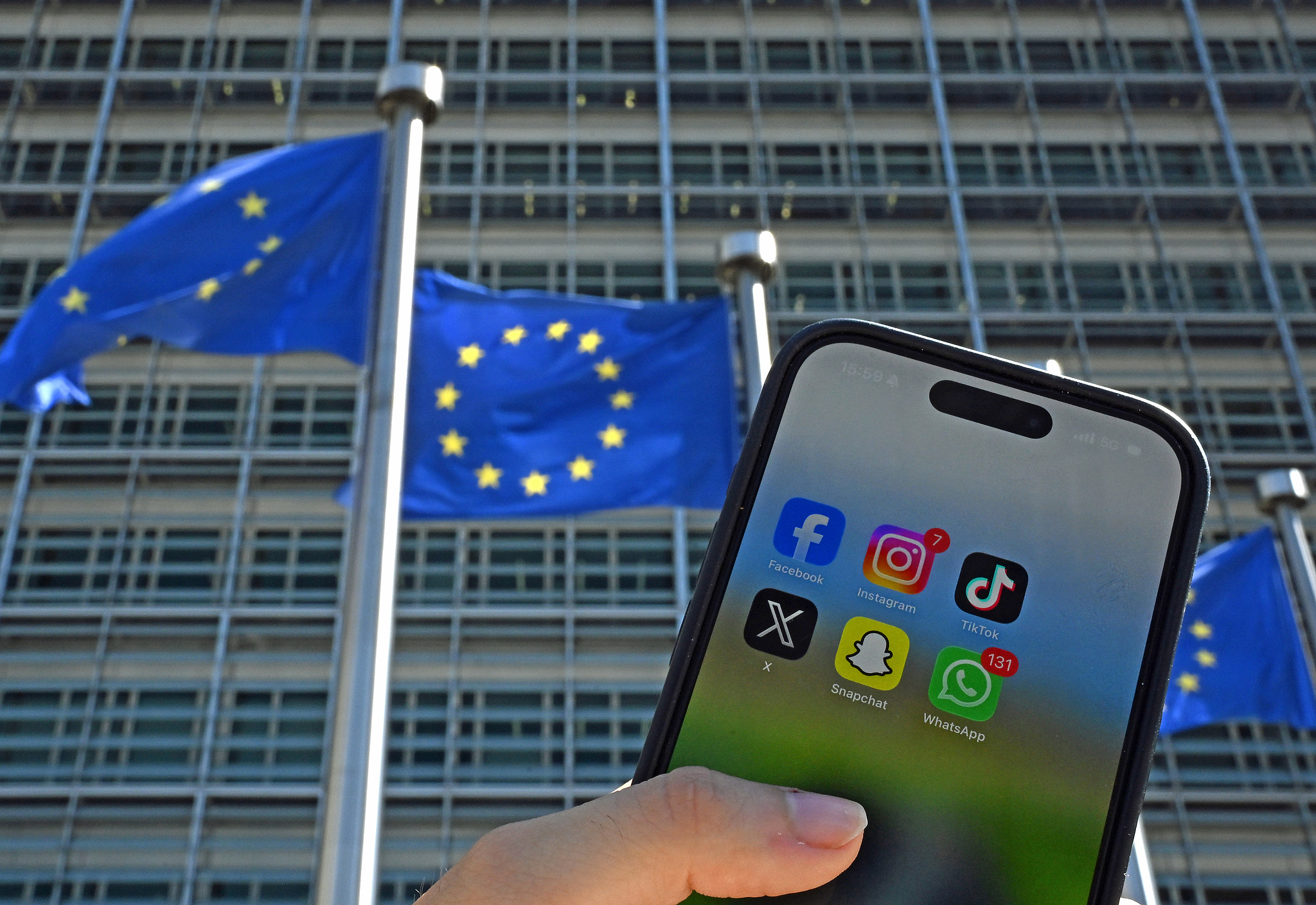 A person holds a smartphone with the logos of the social media apps in front of flags of the European Union and the European Commission building, Brussels, Belgium, May 22, 2026. /VCG