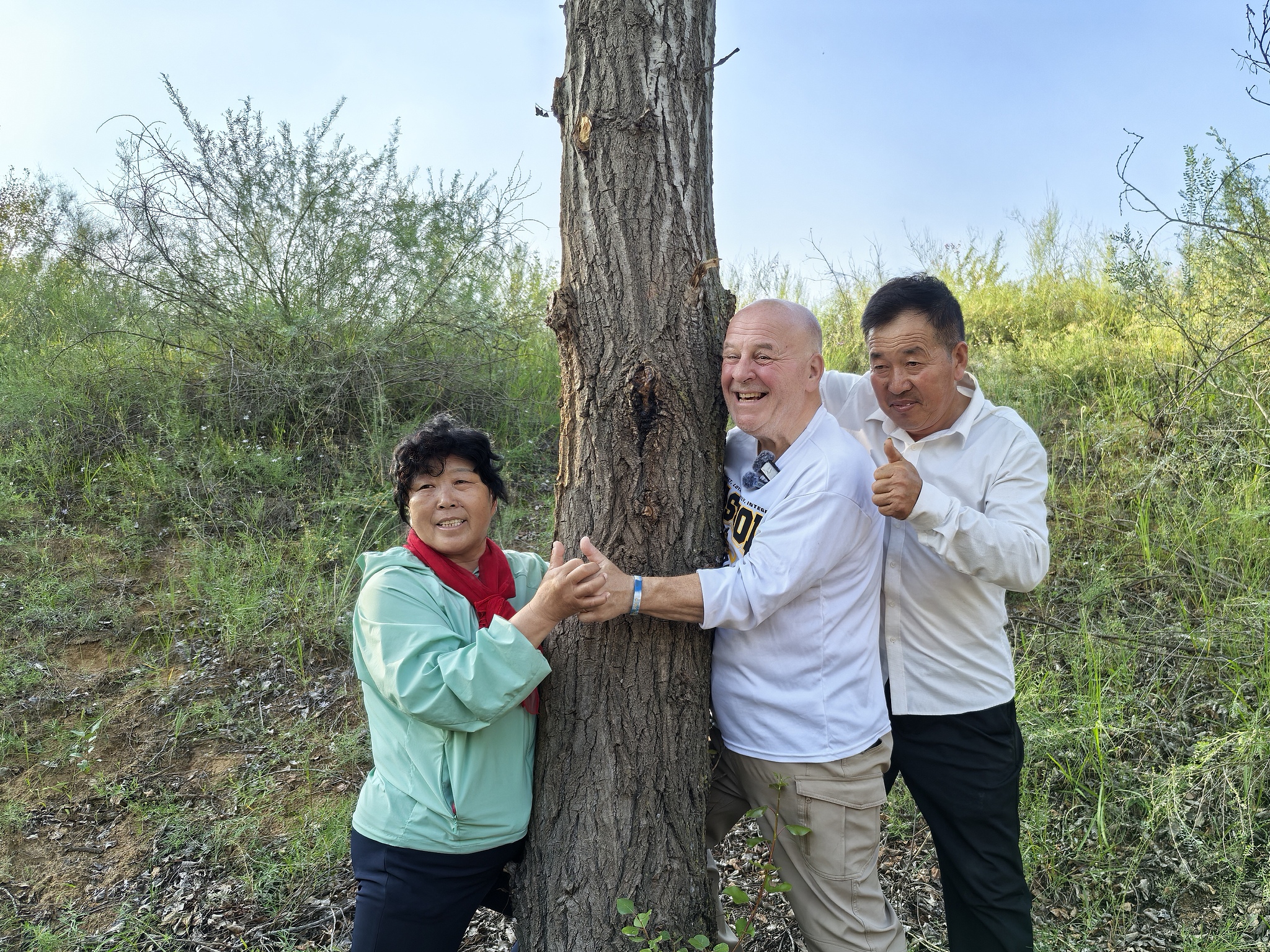 Chinese farmer Yin Yuzhen, left, and retired American teacher Ronald Sakolsky, center, pose for a photo with a tree they had planted 26 years ago, in Ordos, Inner Mongolia Autonomous Region, August 24, 2026. /CFP
