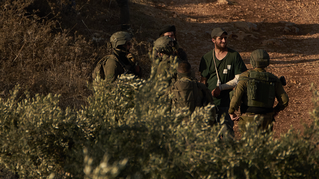 Israeli settlers stand with members of Israeli forces as they gather in an area of a Palestinian olive grove in the West Bank village of Abu Falah, October 6, 2026. /VCG