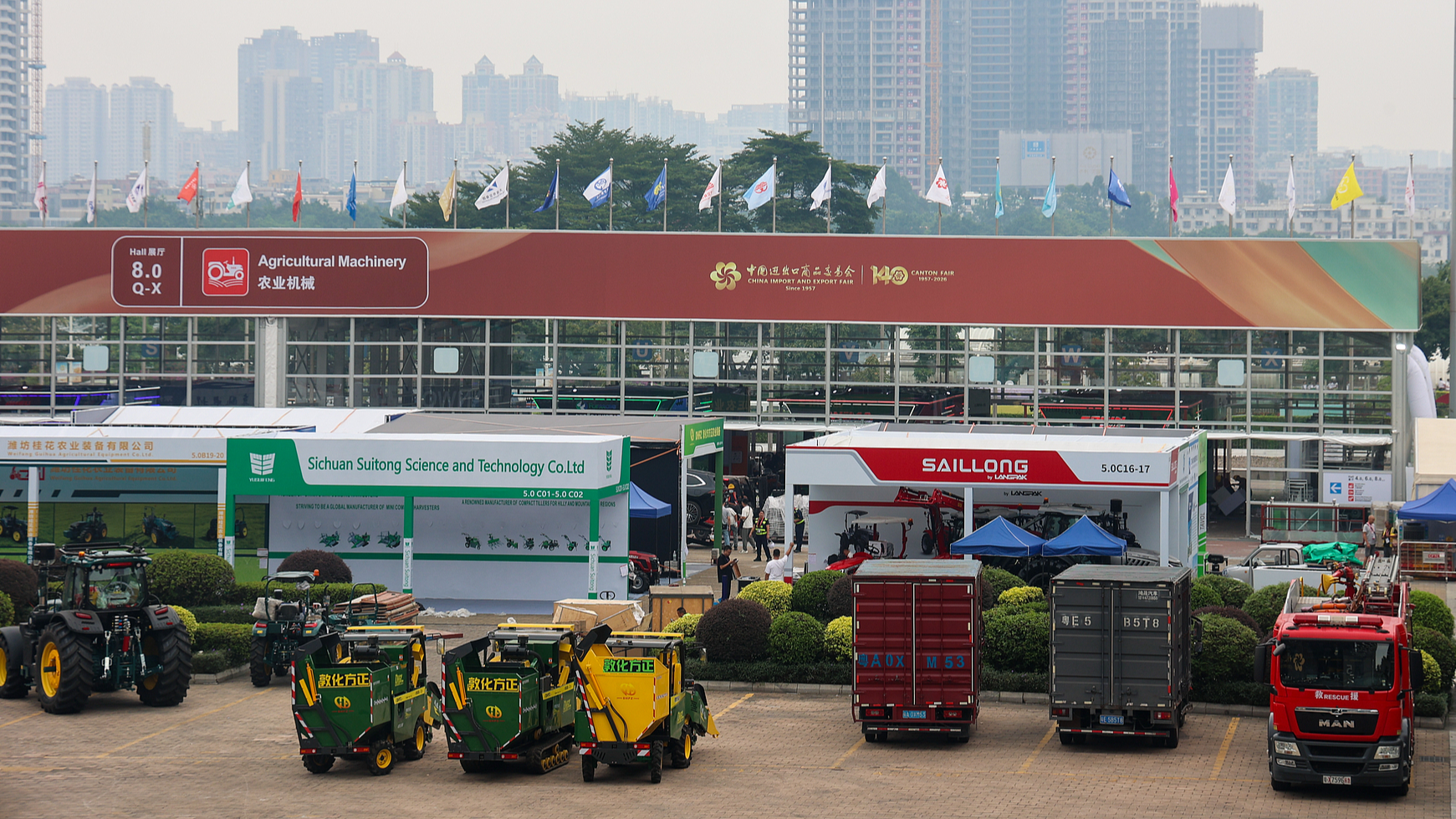 Agricultural machinery and trucks are displayed beneath a sign reading 