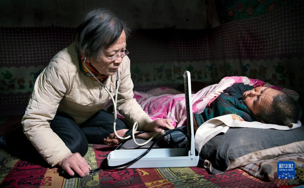 Lu Shengmei (left) kneels on a traditional earthen kang bed to provide a free medical consultation to paralyzed villager Qiao Aifen in her cave dwelling in Hejiagou Village, Dian Town, Jiaxian County, Shaanxi Province, January 18, 2021. /Xinhua